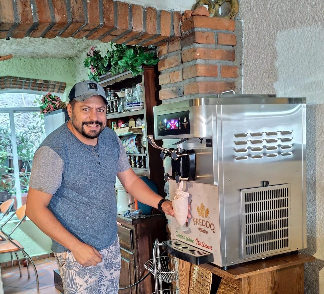 Hombre sonriendo junto a la máquina de gelato mientras sirve un vaso